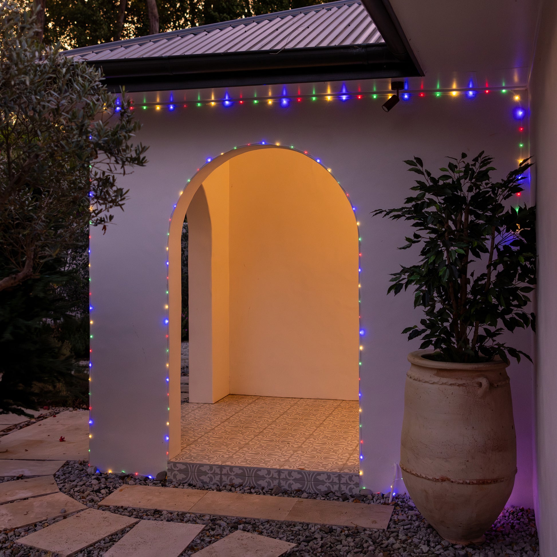 Multicoloured solar rope lights strung around a house and archway at dusk