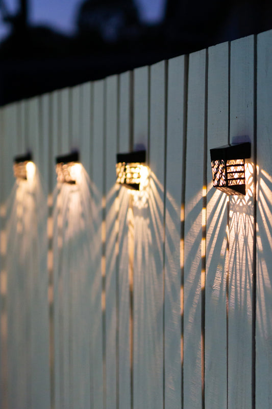 Set of four patterned solar wall lights mounted on to white fence