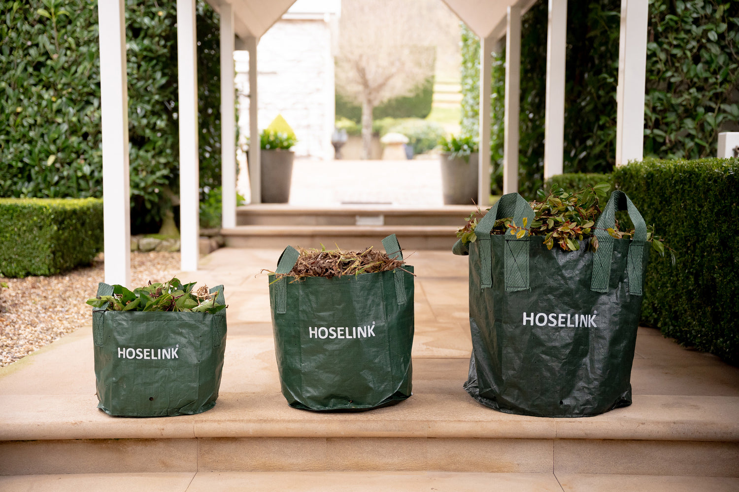 Hoselink's three planter bag sizes side by side on a step all filled with leaf litter and garden debris
