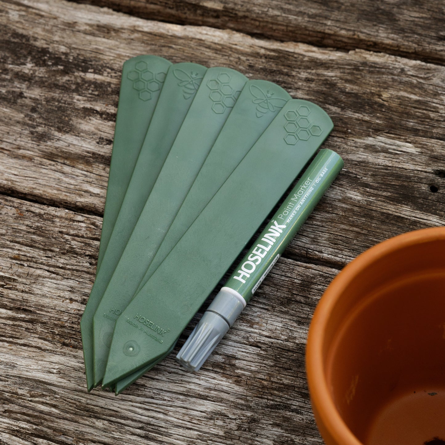 Set of five recycled plastic plant labels next to a Hoselink marker pen on top of a wooden bench with a terracotta pot