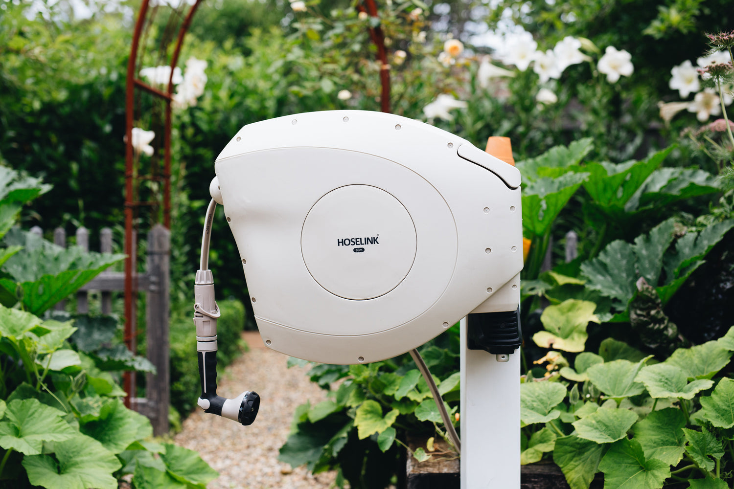 Beige Retractable Hose Reel on Mounting Post Surrounded by Plants