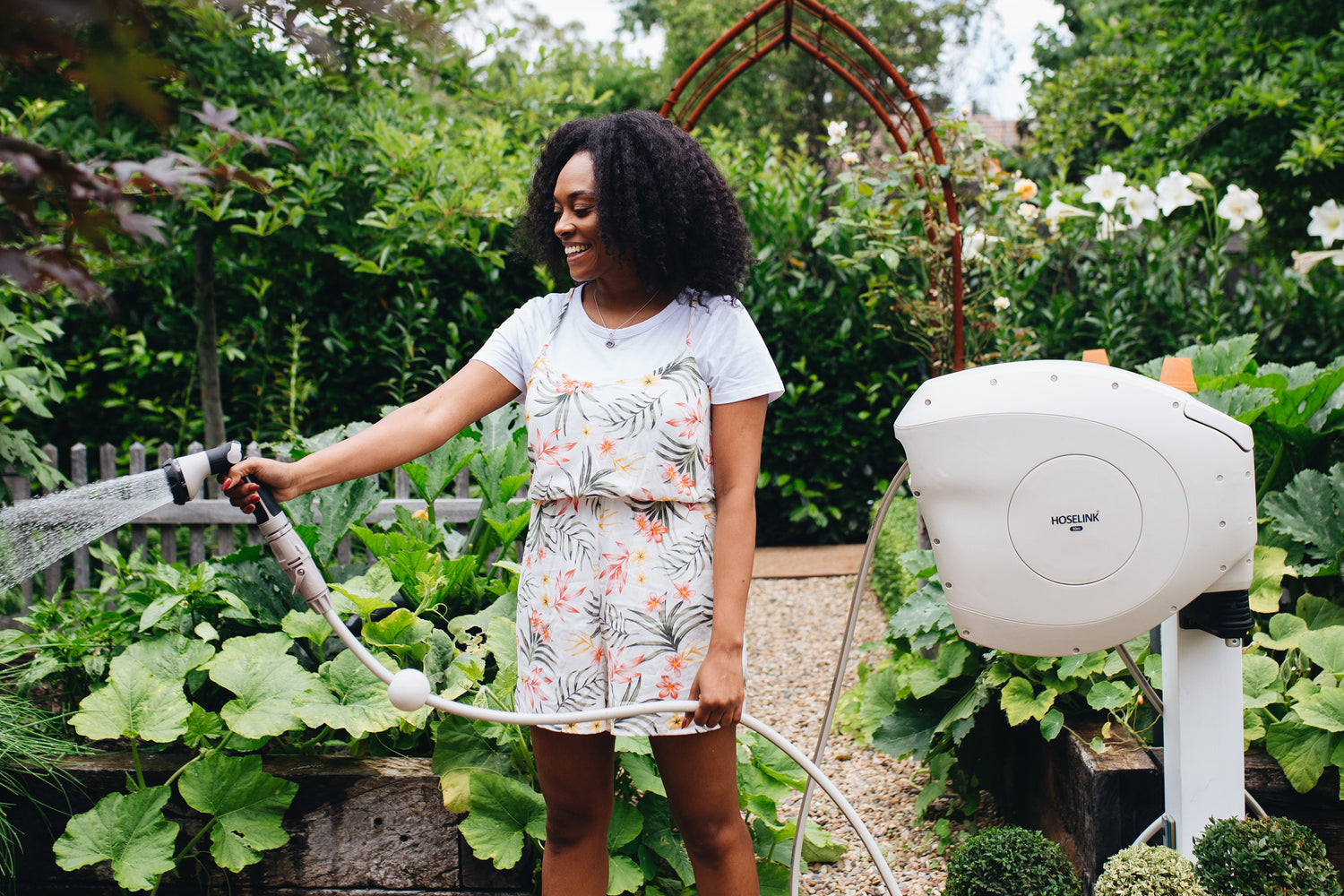 Charcoal Retractable Hose Reel on Mounting Post Being Used By Woman To Water Her Vegetable Garden