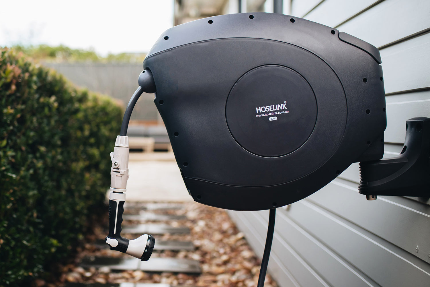 Charcoal Retractable Hose Reel Mounted On Cladding On The Side Of a House