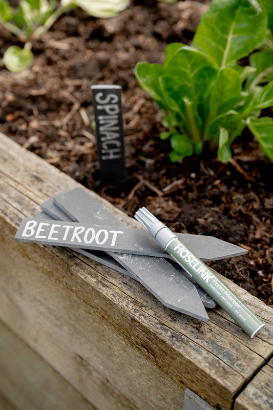 Pile of slate plant labels on edge of raised garden bed with marker pen resting on top