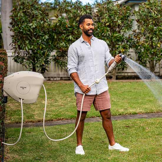 man using beige retractable hose reel to water the lawn