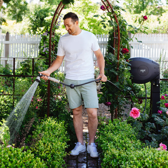 man using charcoal retractable hose reel to water the garden 