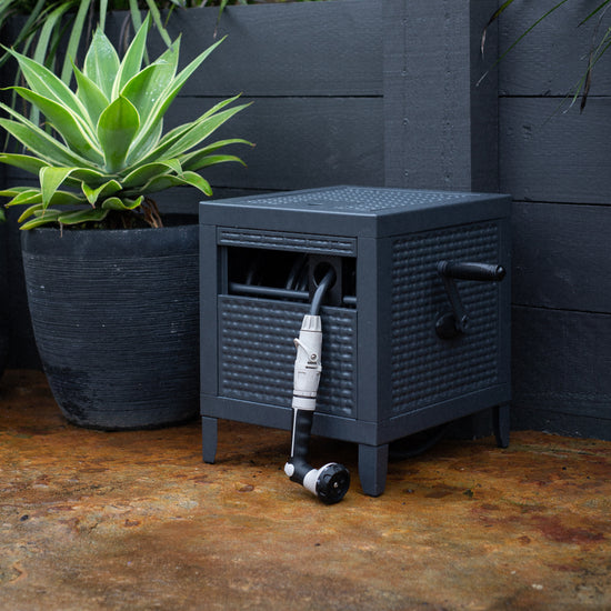 charcoal metal hose reel box in garden with pot plant next to it 