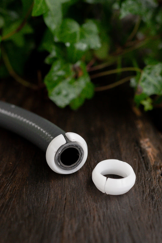 Two white plastic split rings on a table. One is on the end of a 12mm hose and the other is lying next to it
