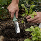 Person using a stainless steel garden knife tool to plant a seedling in soil