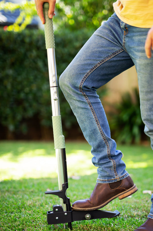 mans foot leaning on stand up weed puller to pull weeds from lawn