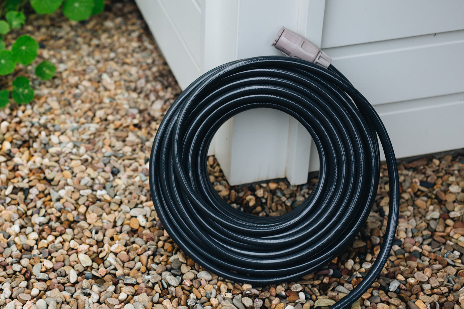 Charcoal Superflex Garden Hose coiled in a circle leaning against edge of glasshouse in garden