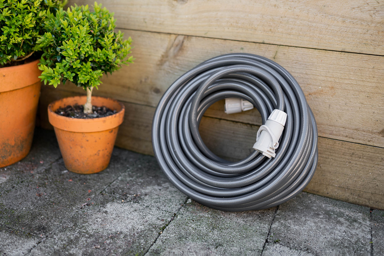 Charcoal Superflex Hose coiled neatly leaning against wooden wall with two pot plants on the left