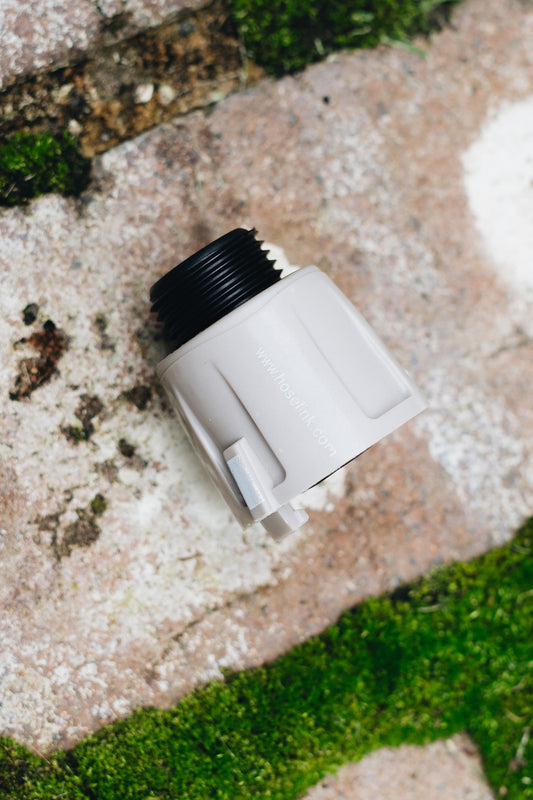 Warm grey US Thread Caravan Connector with black three quarter inch thread laying on sandstone brick pavers and moss