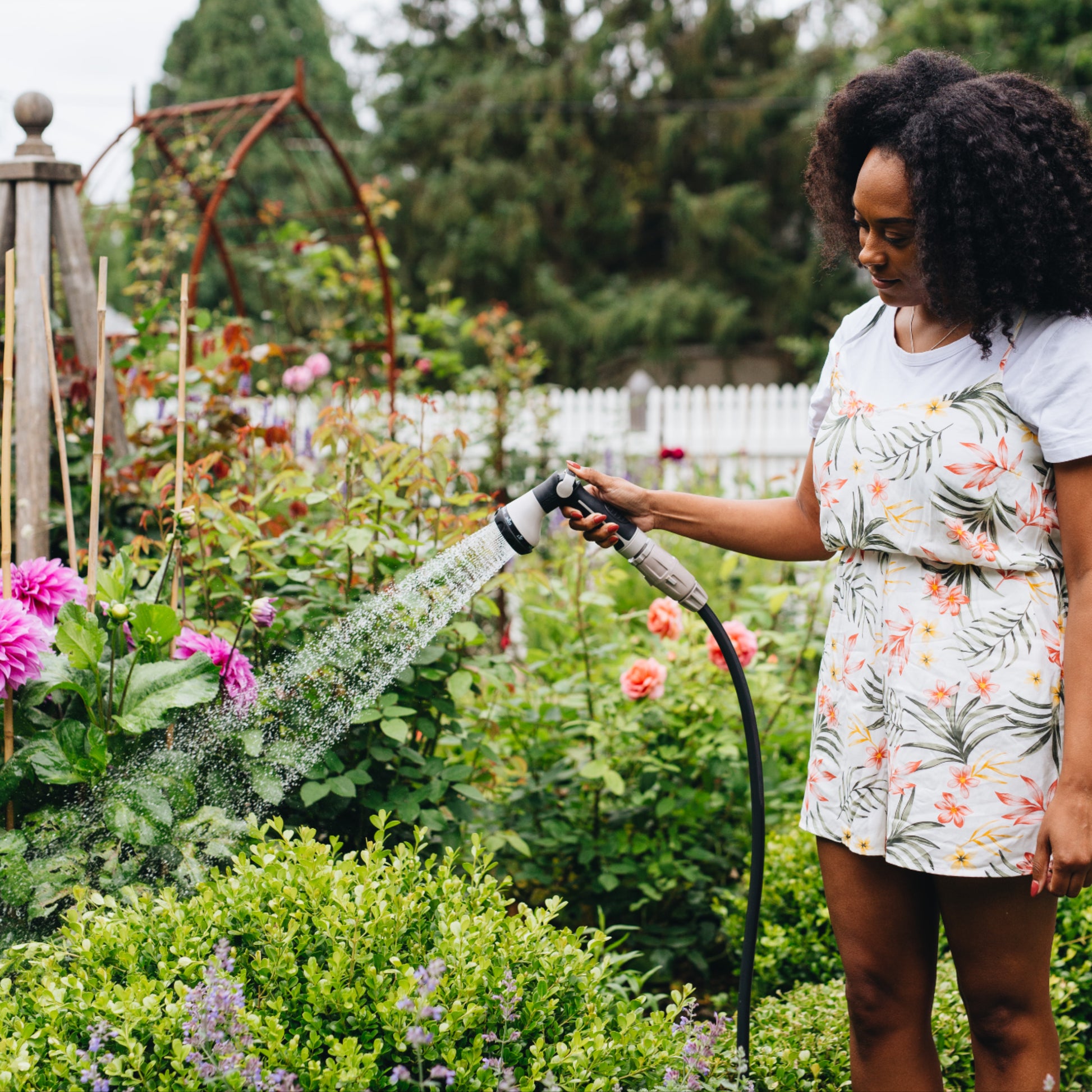 Woman watering plants in a garden with a charcoal hose and grey spray gun