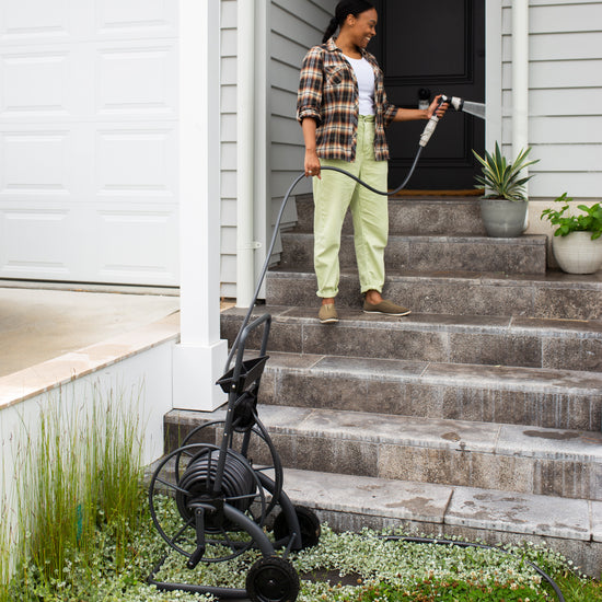 woman standing on steps above charcoal hose reel cart and watering plants