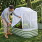 A person opening-the mesh cover attached to a 6 in 1 garden bed in front of a hedge