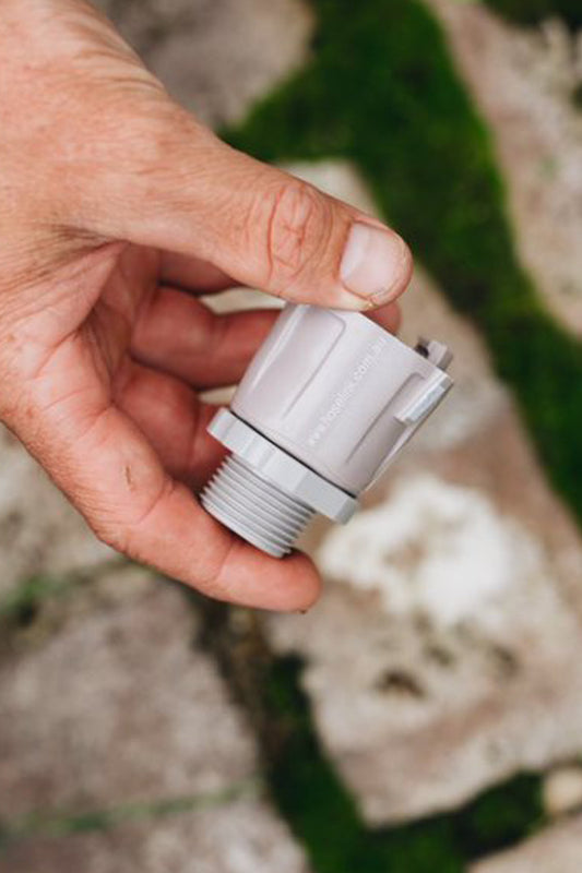 Warm grey Accessory Connector with Swivel being held above sandstone pavers and green moss. 