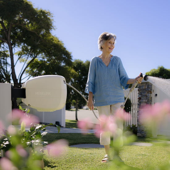 woman in blue top and white pants water the lawn with a beige Evolve retractable hose reel