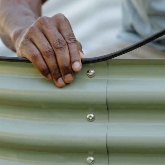 Close up of hand attaching black safety strip the the top edge of a metal garden bed