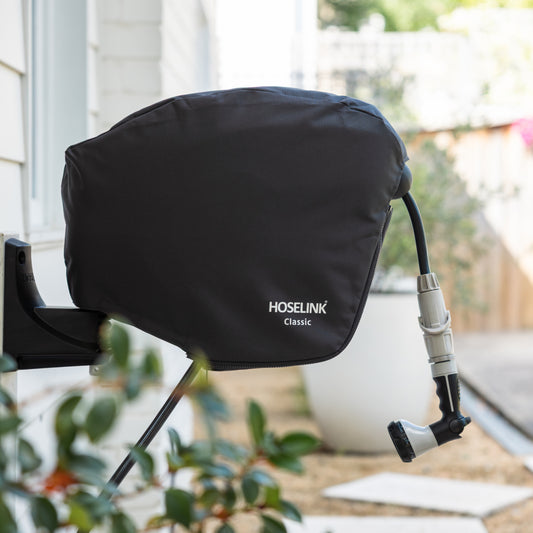 Charcoal Hoselink hose reel cover with white logo fitted to reel attached to a wall with plants and steps in the background.