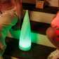 Tall Solar Santa light, sitting on some wooden stairs in between two little kids. The Tall Solar Santa light is emitting a green glow. 