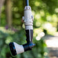 A close-up of Hoselink connectors including an Accessory connecto, Hose end with flow control and 8-pattern spray gun hanging outdoors on a hose against a blurred green garden background. The nozzle has a white and black body with a charcoal hose connected at the top.