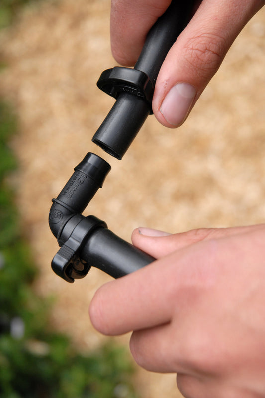 close-up of someone installing 13mm elbw joint into irrigation tuning with straw mulch in the background