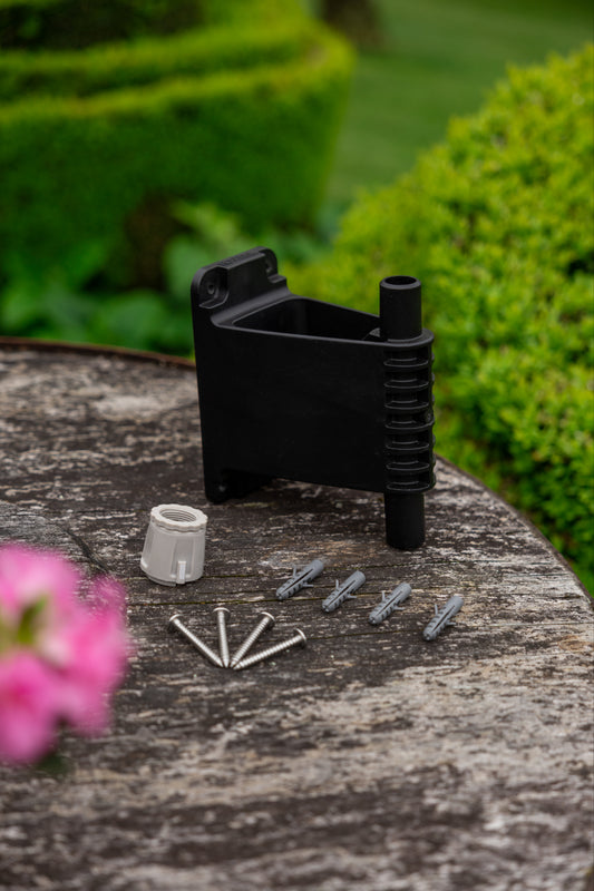 Evolve wall bracket, screw, plugs and Universal Tap Connector on a wooded table with green hedges in the background