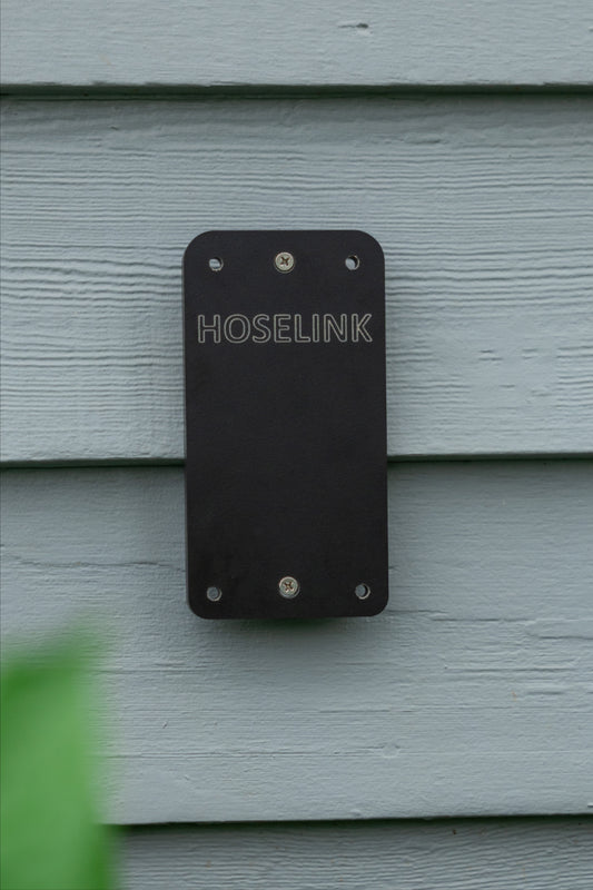 Black Evolve Hose Reel Backing Board with Hoselink logo mounted with two screws on a steel blue weatherboard wall