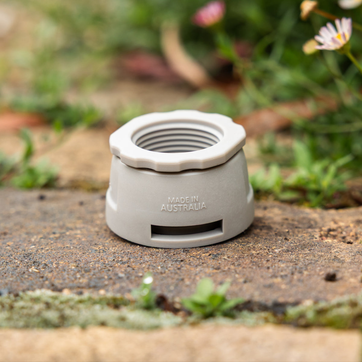 Close up of Gen 2 Universal Tap Connector with reducer. Resting on brown paving with blurred flowers in the background