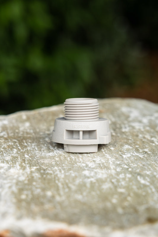 A gray plastic accessory connector, shown sitting on a textured stone with a blurred green garden background.