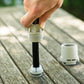 A close-up of a hand installing a charcoal hose with white plastic split-ring onto hose end connector stem on a wooden table