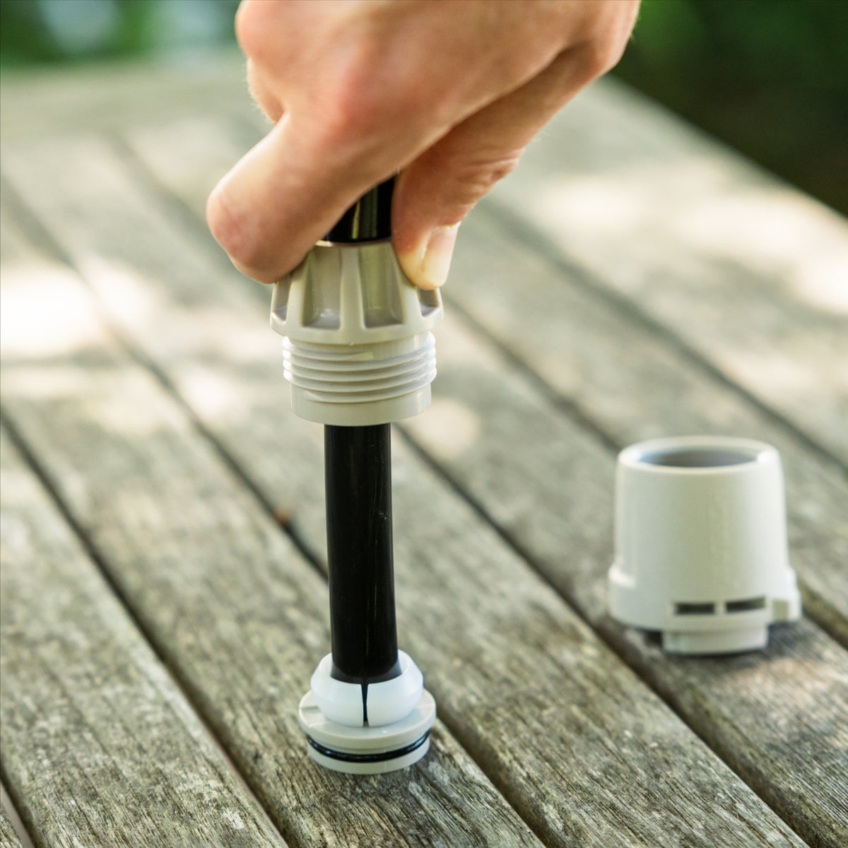 A close-up of a hand installing a charcoal hose with white plastic split-ring onto hose end connector stem on a wooden table