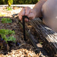 Person installing a black irrigation hold down spike into a garden bed filled with soil and straw mulch
