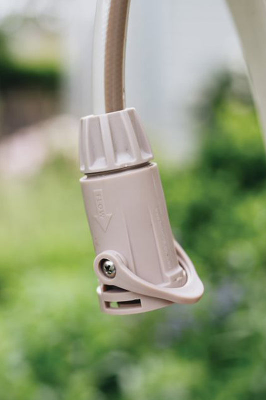 Warm grey Hose Connector with Flow Control hanging from a white hose with an out of focus garden in the background. 