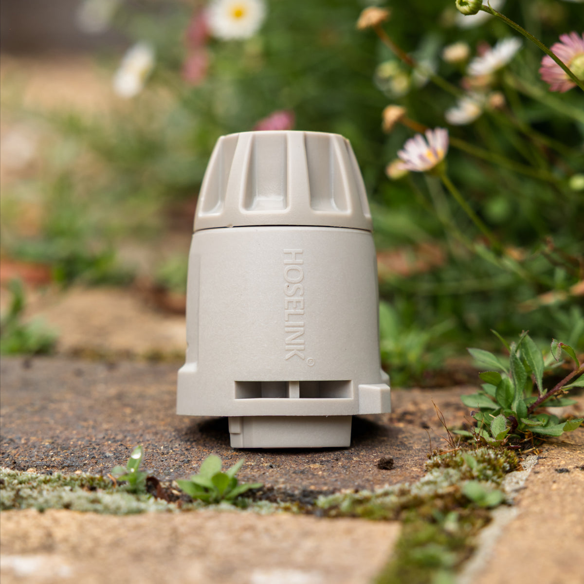 A HOSELINK Hose End Connector standing on a stone path with blurred flowers and greenery in the background.