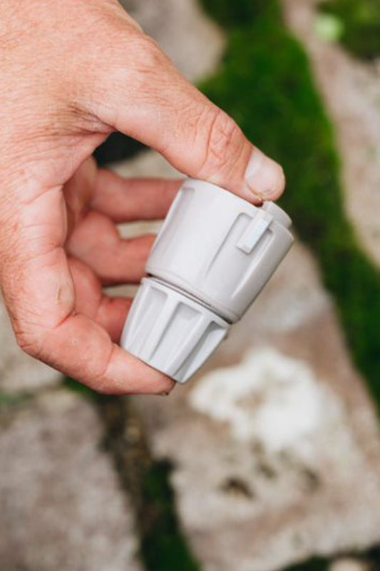 Warm grey Hose End Connector being held above sandstone pavers and green moss. 