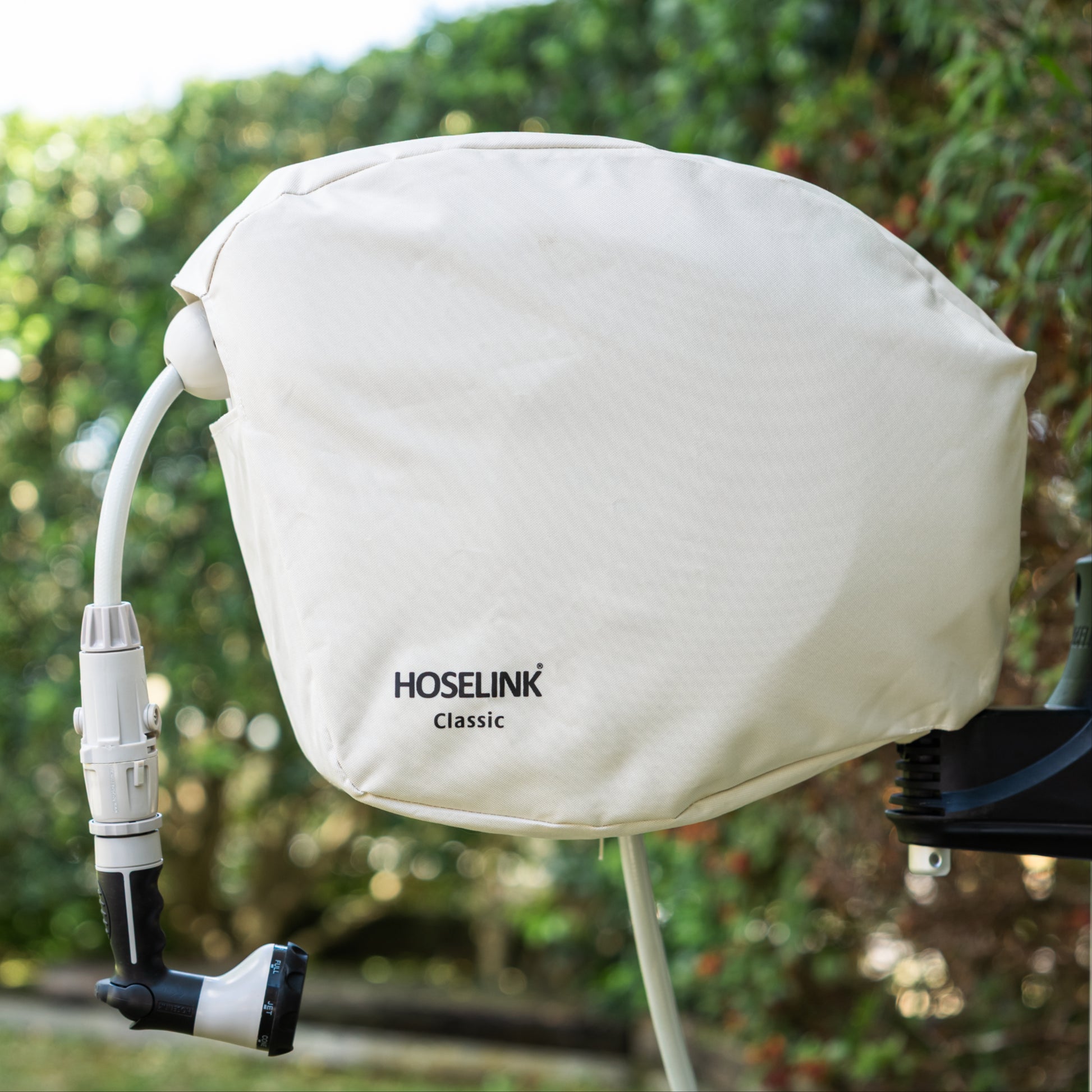 Beige classic hose reel cover with black Hoselink logo on a hose reel in a backyard with green lawn and hedges in the background