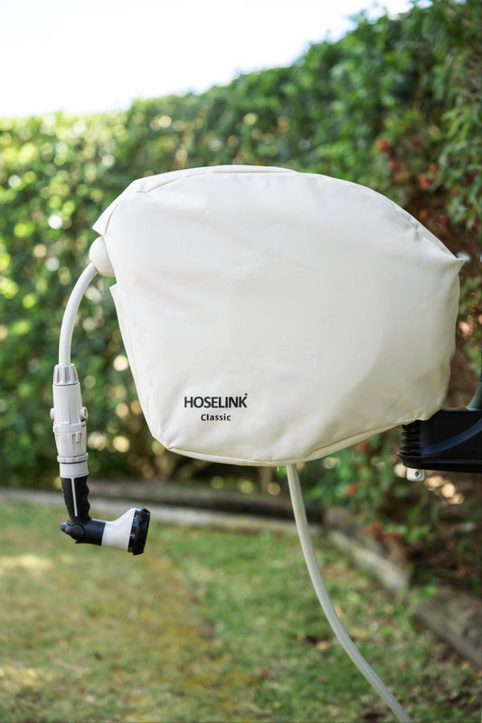Beige classic hose reel cover isntalled on a Hoselink hose reel in a backyard with green lawn and hedges in the background