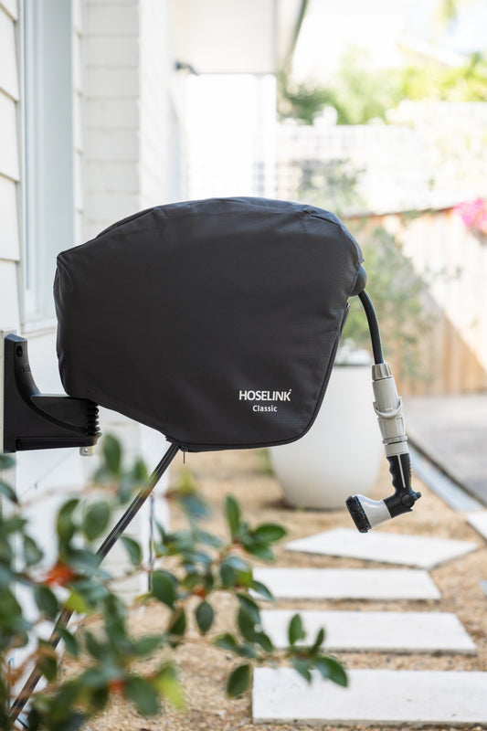 Charcoal Hoselink garden hose reel with cover attached to a wall with plants and steps in the background.