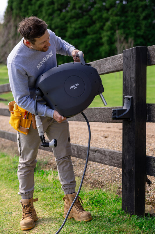 Ben Heyman lifting a charcoal classic retractable hose reel into the mounting bracket on a dark wooden post