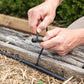 person fitting irrigation micro tubing to a drip head along the edge of a wooden garden bed with a green hedge in the background