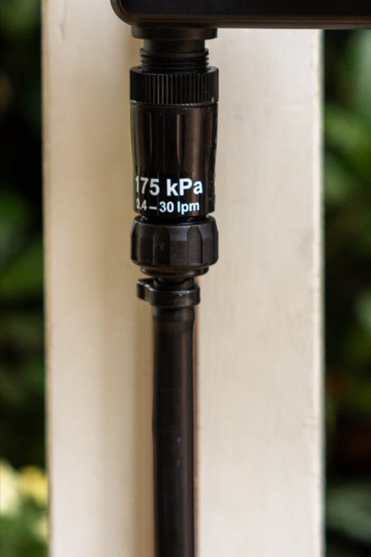 Close-up of an irrigation kit nut & tail connecting irrigation tubing to a pressure regulator on a white