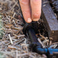 Cloes-up of a hand pushing the top of an irrigation hold down spike over poly pipe in a garden bed with soil