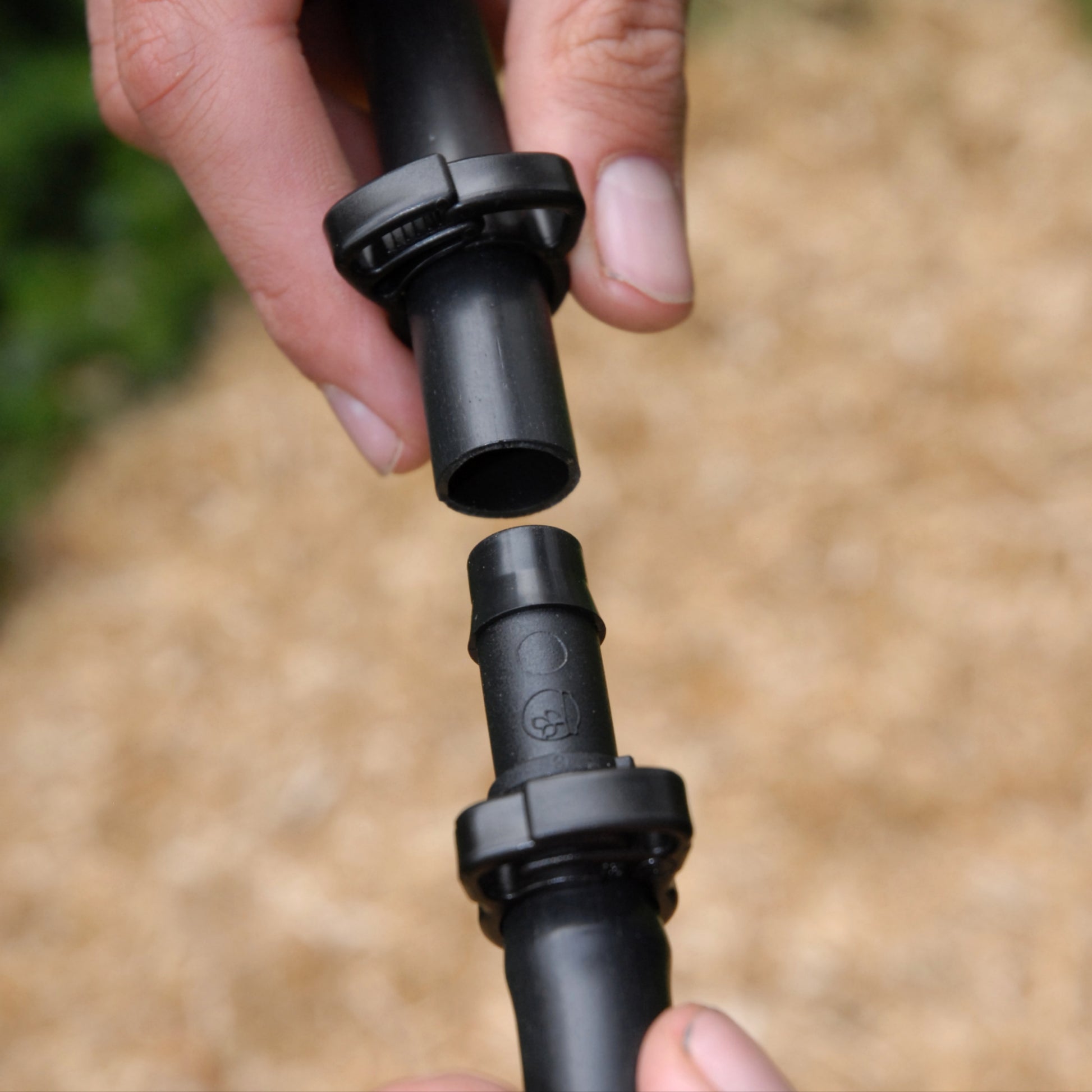 close-up of hands installing a 13mm irrigation joinr to a piece of black poly pipe with ratchet clamps