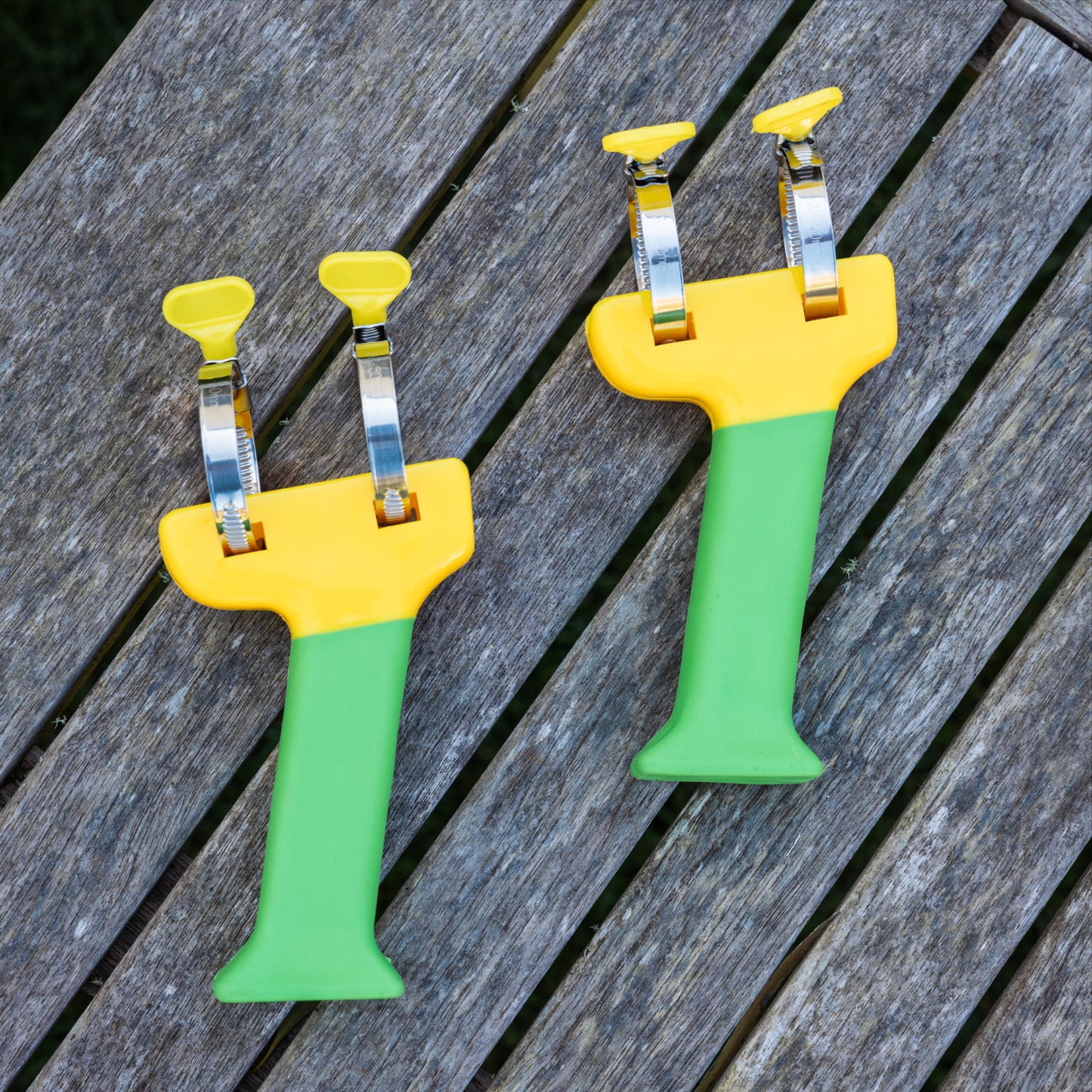 Pair of green and yellow PETA Easi Grip Add-On Handles lying on a wooden deck, untreated.