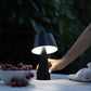 Indoor-Outdoor-Table-Lamp on picnic table next to a bowl of grapes, woman's hand is place on the stem of the light