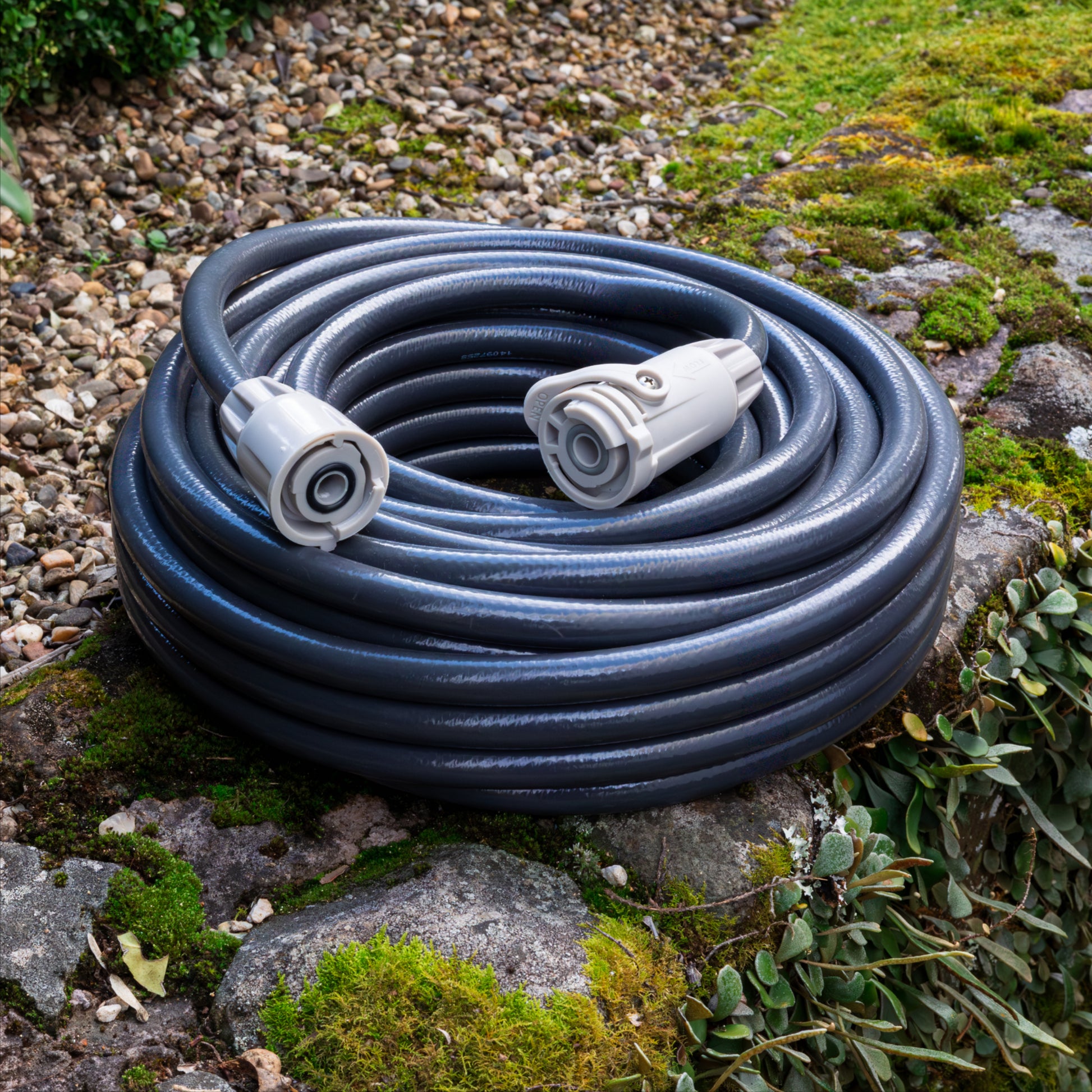 Coiled garden hose with connectors on a stone, mossy surface