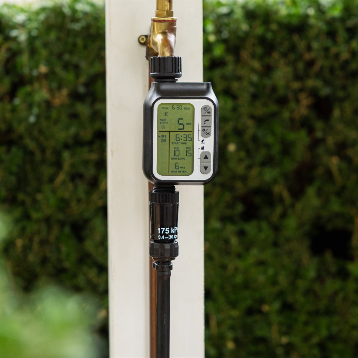 Black pressure regulator and tap timer atatched to a brass tap on a white post