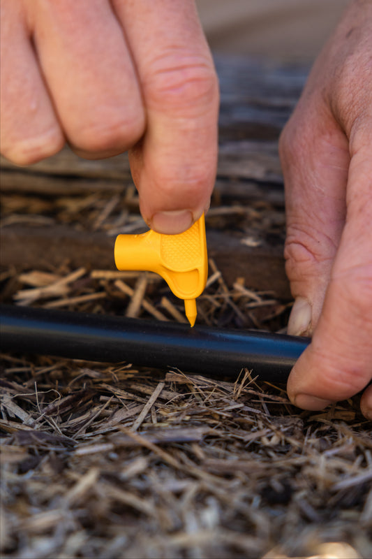 Person using a yellow key punch to create a hole in black pipe in a natural settinge
